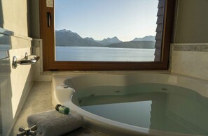 A bathroom with a bathtub, a window, and a view of a lake and mountains. - El Faro Boutique Hotel & Spa by DON (Villa La Angostura)