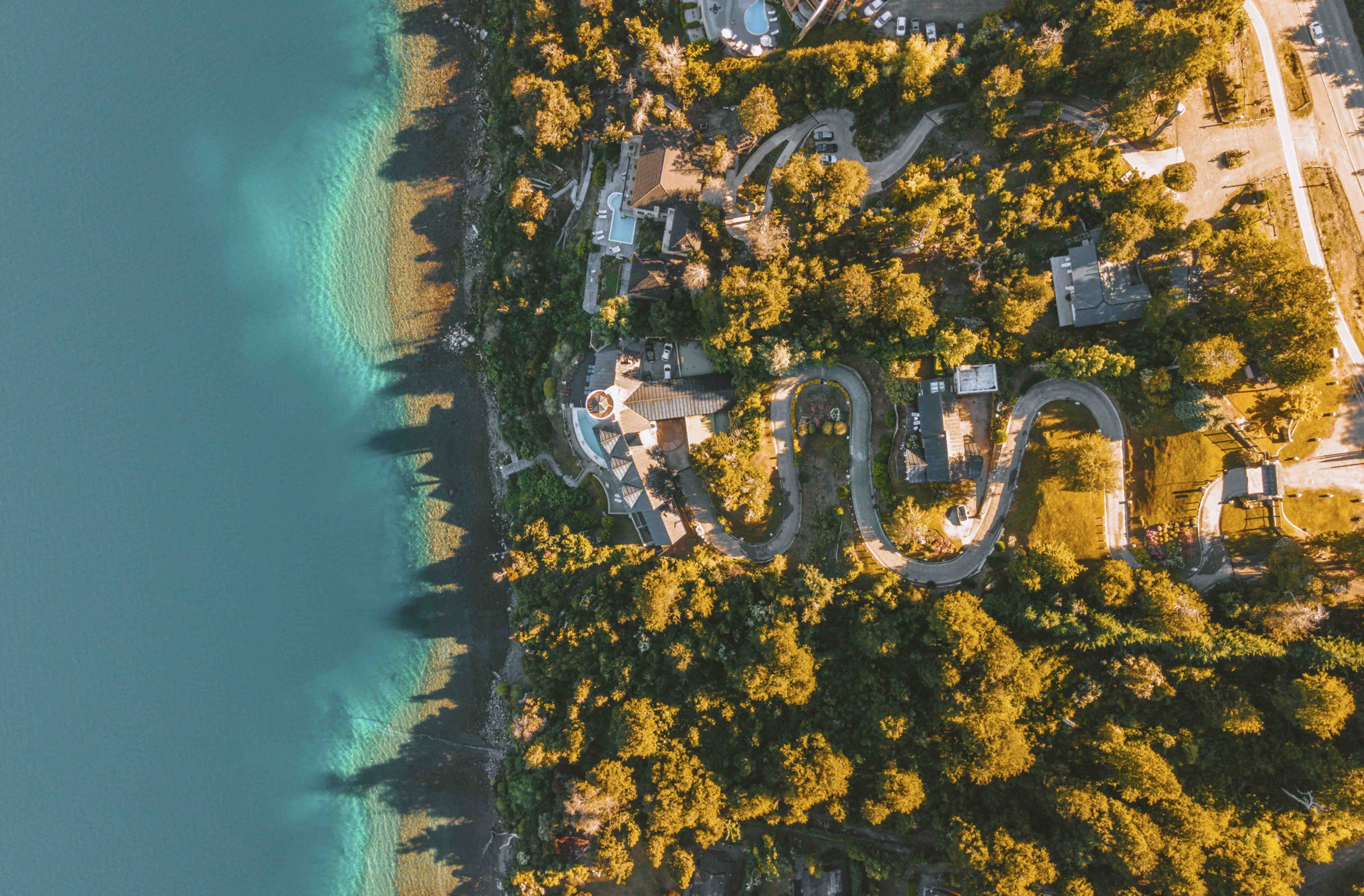 Vue aérienne d’une propriété située sur la côte, avec une route sinueuse, une allée circulaire et une plage.