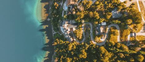 Vue aérienne d’une propriété située sur la côte, avec une route sinueuse, une allée circulaire et une plage.
