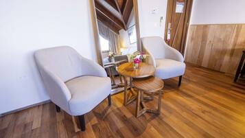 Una habitación con dos sillones tapizados, una mesita de madera con un jarrón de flores y suelo de madera.