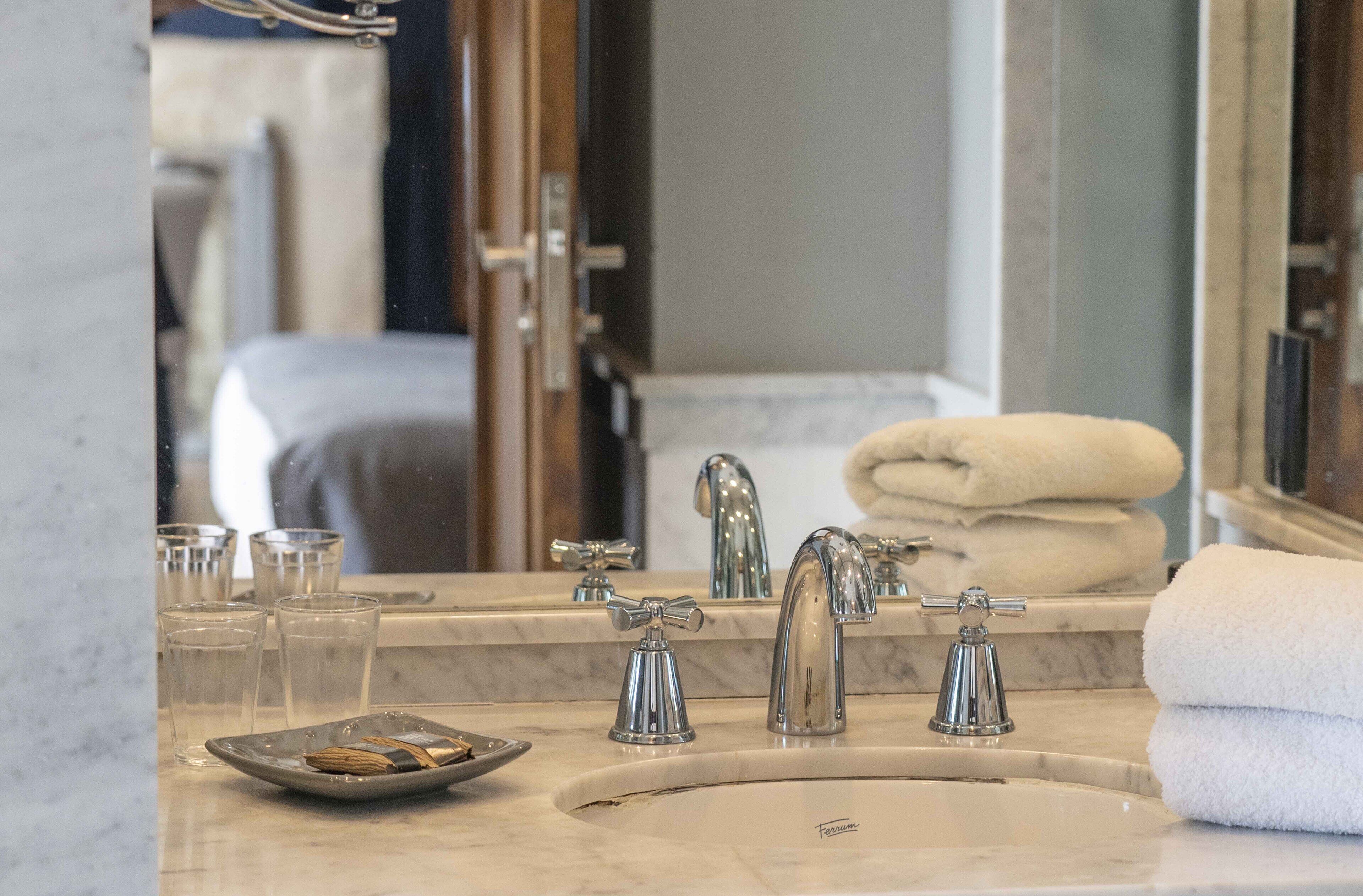 A bathroom with a sink, two faucets, a mirror, and a towel rack.