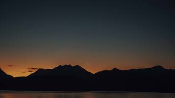 A nighttime landscape with mountains silhouetted against a sky transitioning from dark to light.