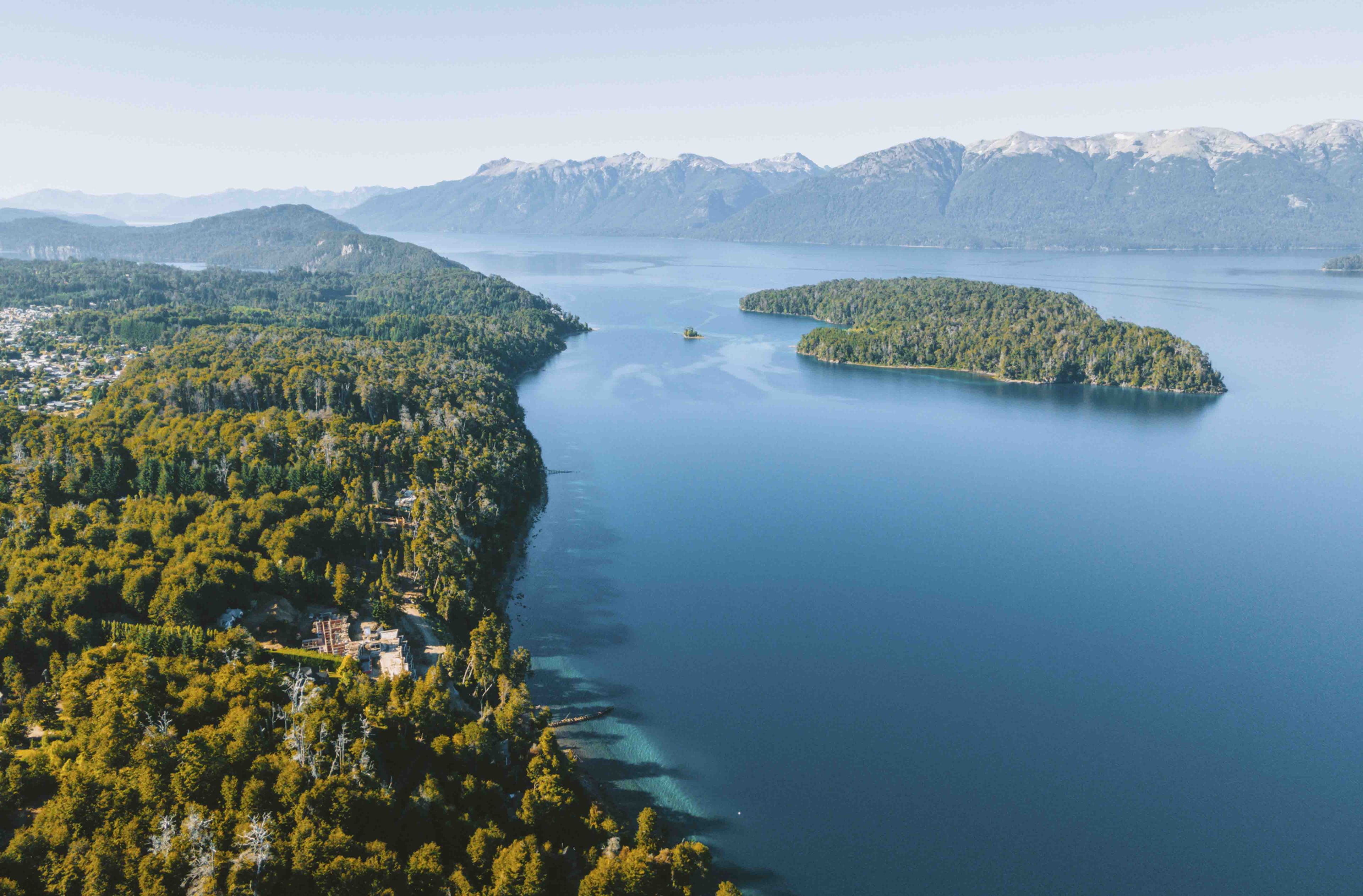 An aerial view of a coastal area with a small island, dense forest, and mountains in the background.