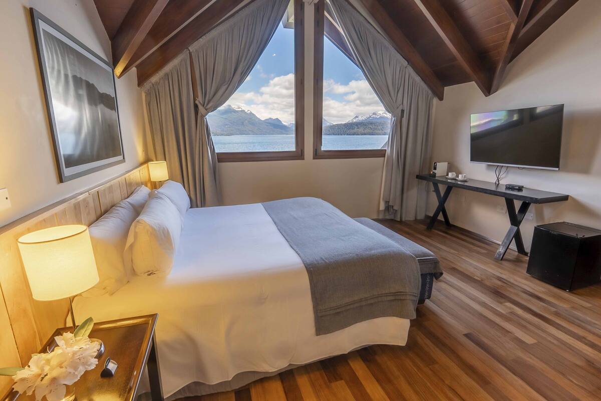 Ett hotellrum med en säng, ett skrivbord, en tv och ett fönster med utsikt över bergen.