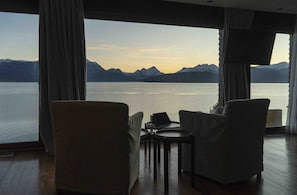 A room with a large window overlooking a lake and mountains. There are two chairs and a small table with a laptop. - El Faro Boutique Hotel & Spa by DON (Villa La Angostura)