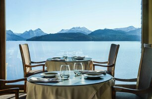 Una mesa de comedor con sillas y vistas a un lago y montañas.