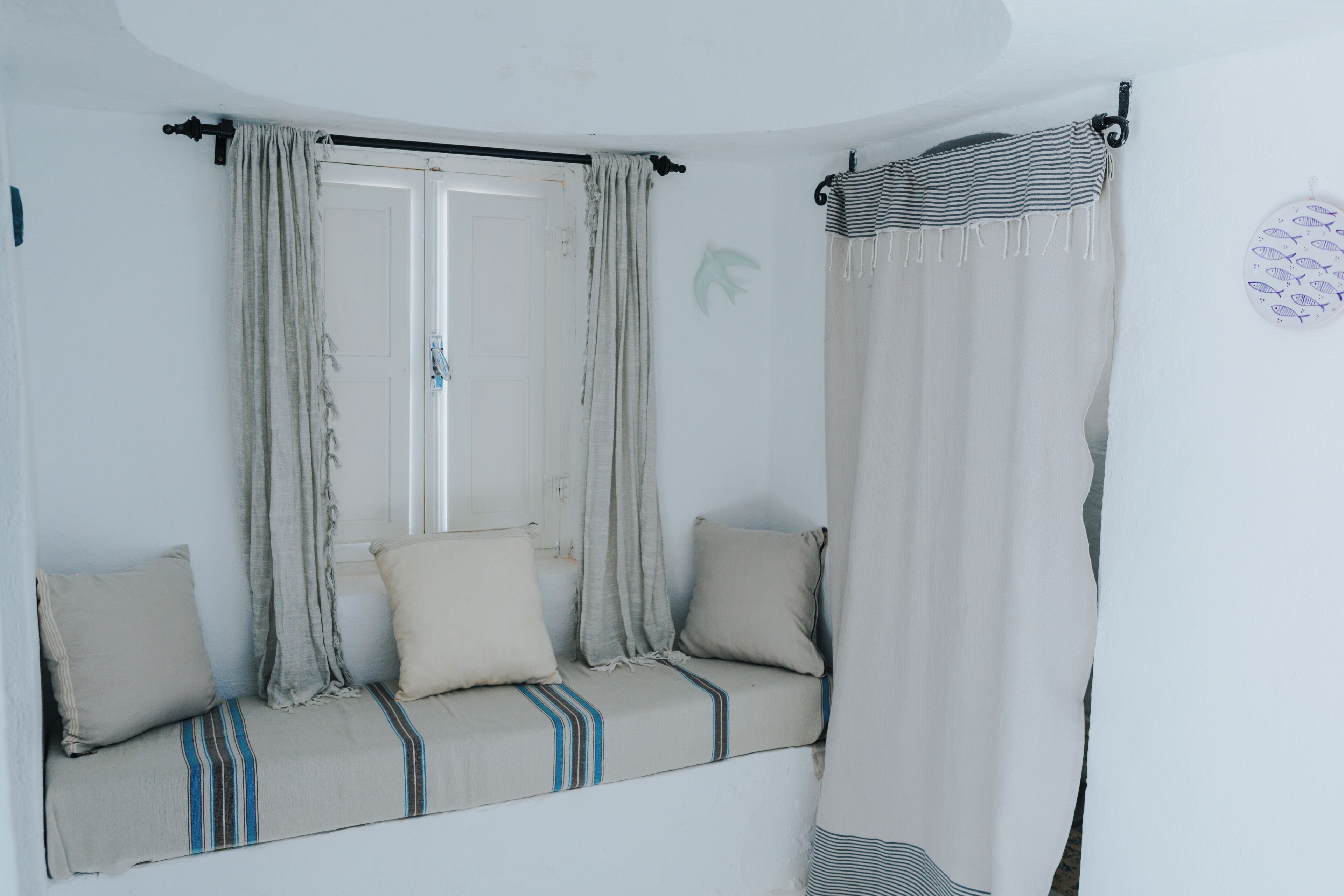 A room with a window seat, curtains, and a wall decoration.