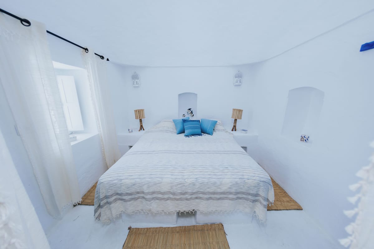 A white room with a bed, a window, and two wall-mounted lamps.