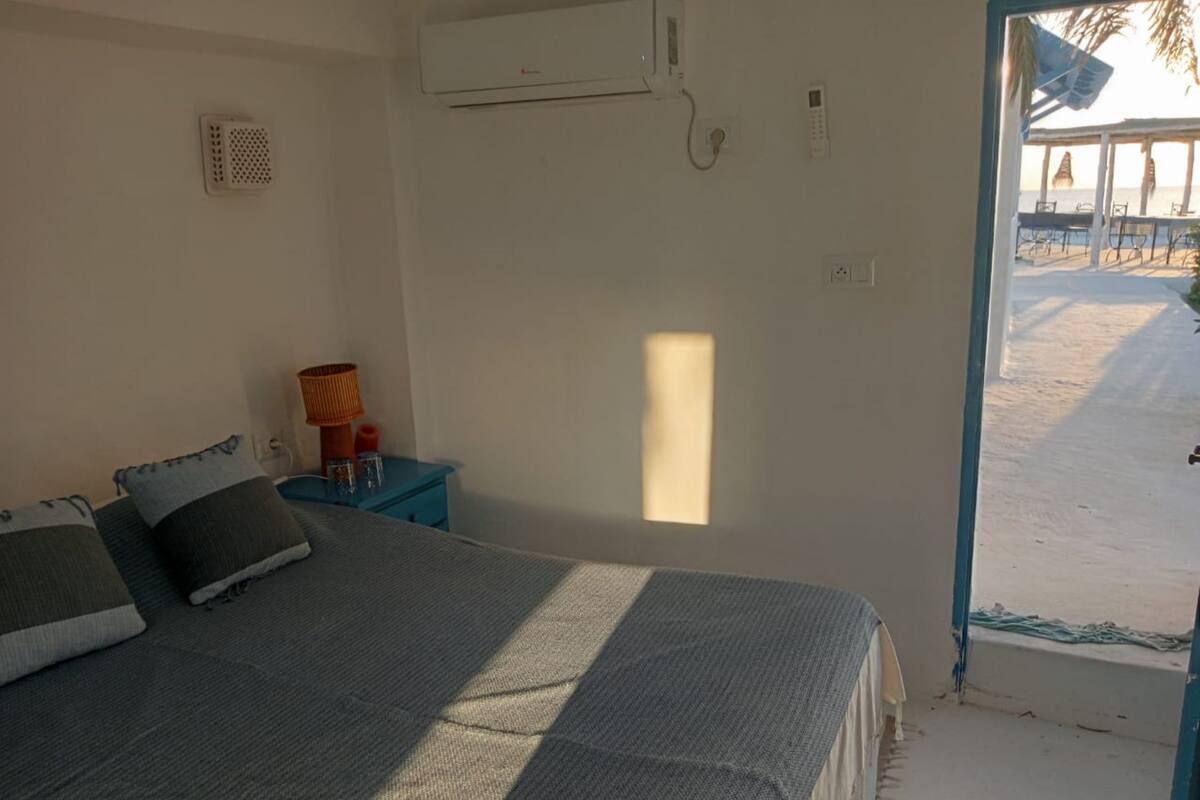 A bedroom with a bed, a nightstand, a window, and an air conditioning unit.