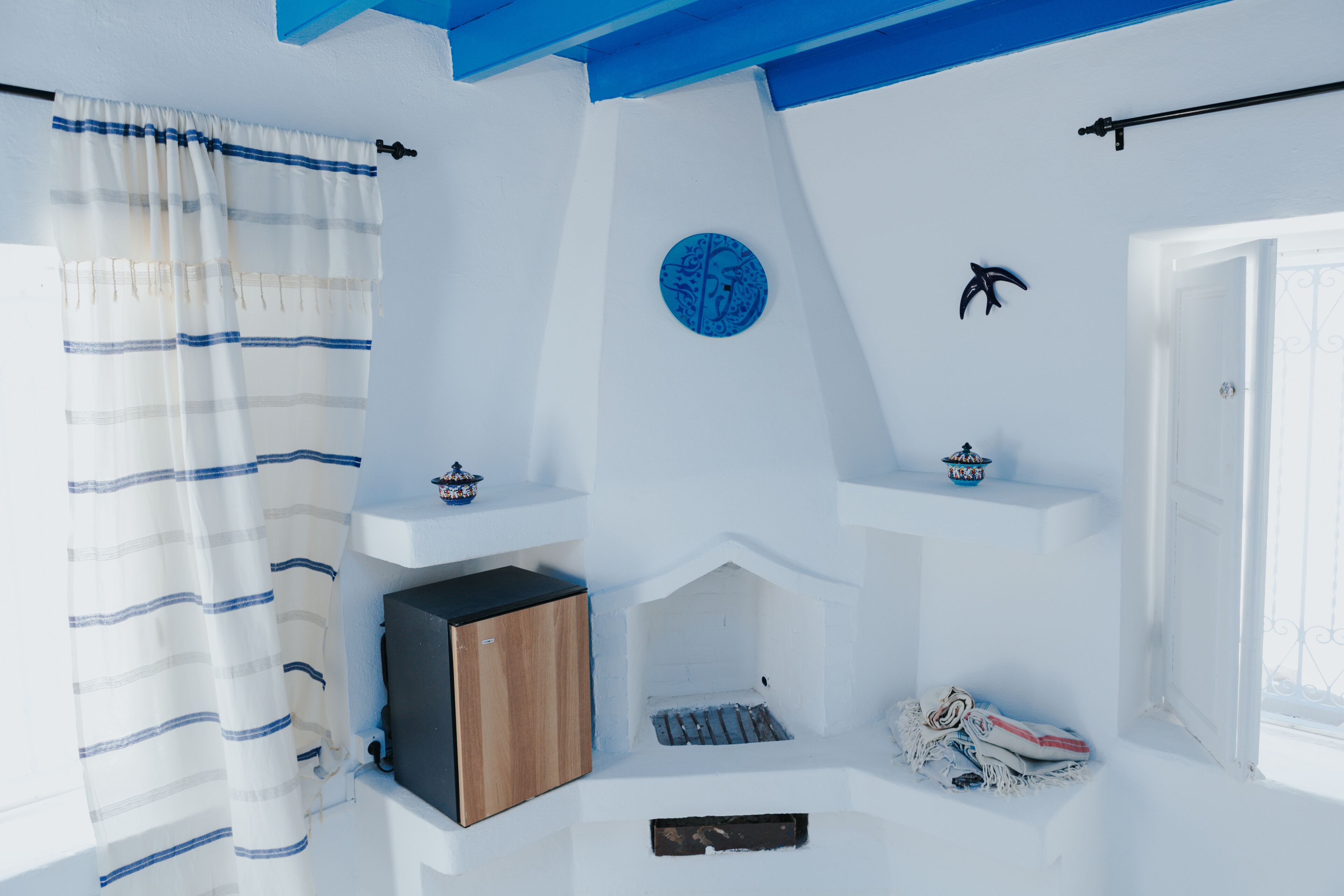A room with a white and blue color scheme, featuring a wooden cabinet, a small shelf with a decorative item, and a window with a view.