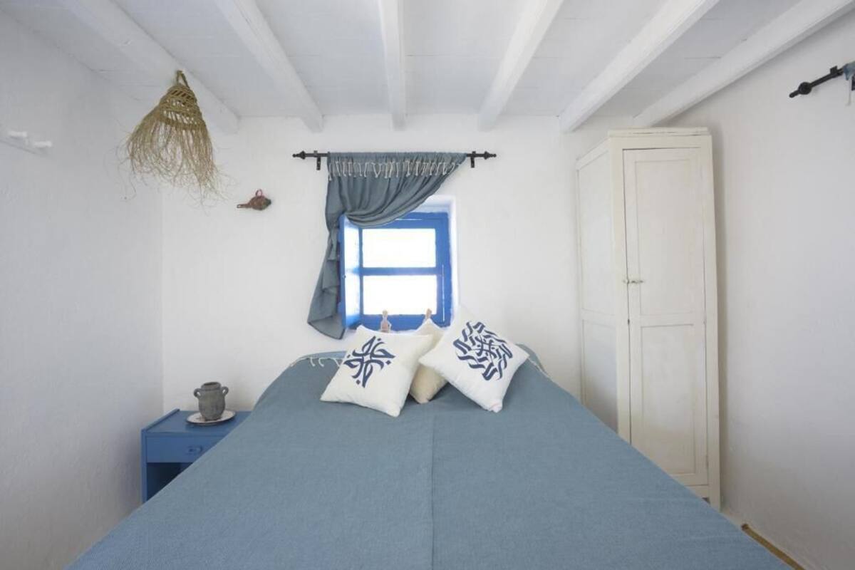 A bedroom with a bed, a wardrobe, a window with curtains, a bedside table with a lamp, and a hanging light fixture.