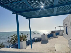 Una terraza costera con vistas al mar, que presenta una pérgola azul, paredes blancas y una barandilla azul.