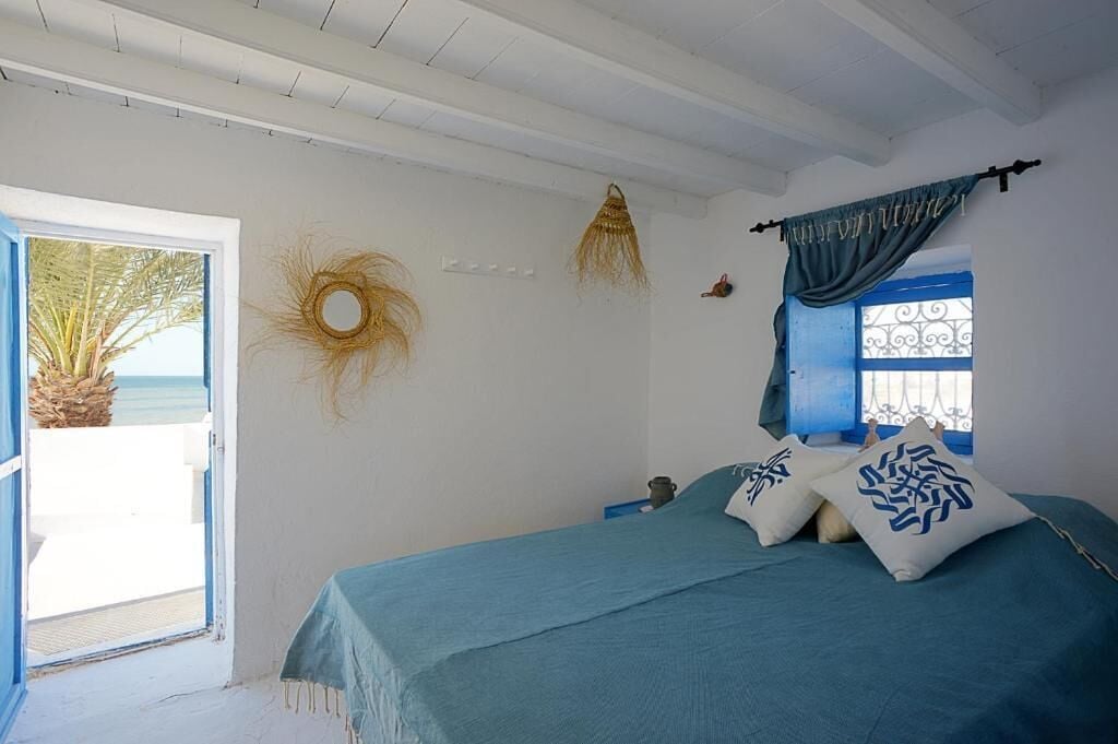 Un dormitorio con cama, una ventana con cortinas azules, una puerta que da a un balcón y un adorno en la pared.