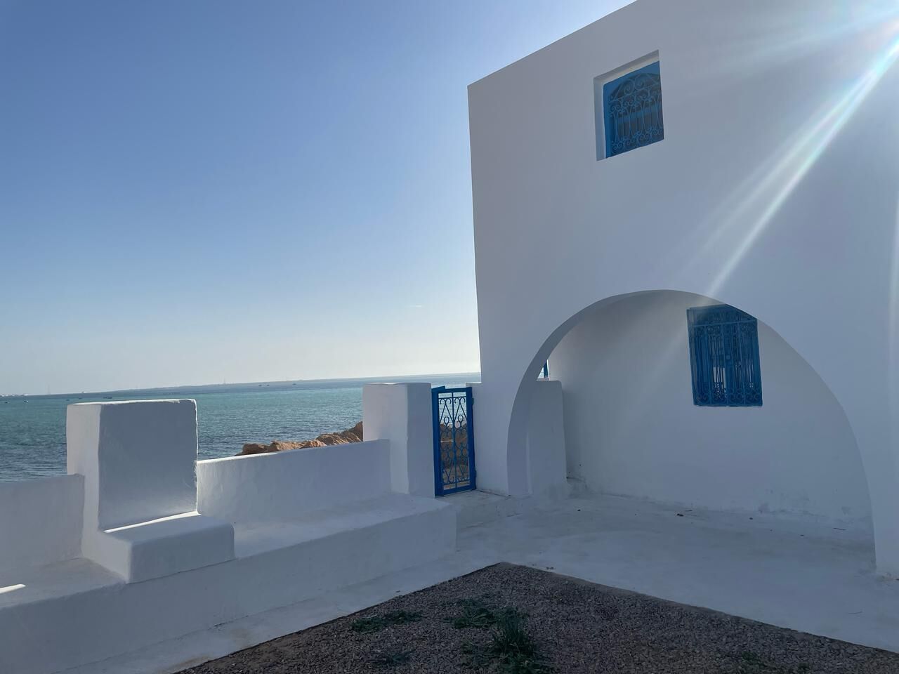 A white building with a view of the sea, featuring a blue door and a small window.