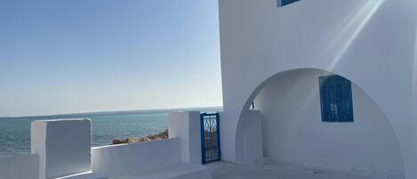A white building with a view of the sea, featuring a blue door and a small window.