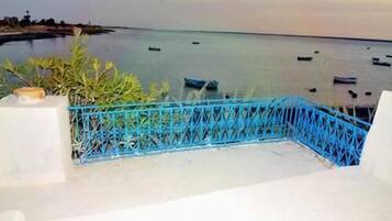 Un balcón con barandilla azul que da a un mar tranquilo con varios barcos.