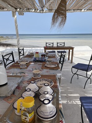 Un montaje para cenar frente al mar, con una mesa dispuesta para dos personas, vajilla tradicional y vistas al océano.