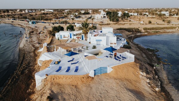Un resort costero con edificios blancos, una playa de arena y una zona de piscina.