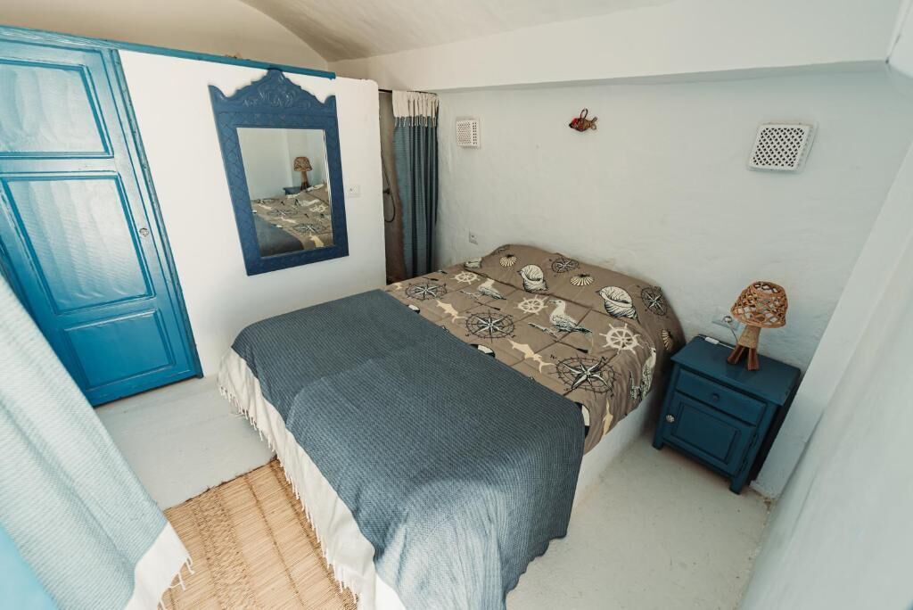 Un dormitorio con cama, un armario azul, una mesita de noche pequeña y un espejo en la pared.