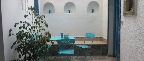 A small patio with a table and chairs, a potted plant, and a wall with decorative arches and shelves.