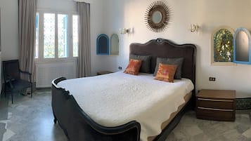 A bedroom with a large bed, a chair, a nightstand, and a window with curtains.