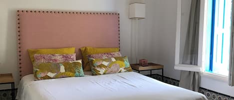 A neatly arranged bedroom with a large bed, a bedside table, a lamp, and a window with curtains.
