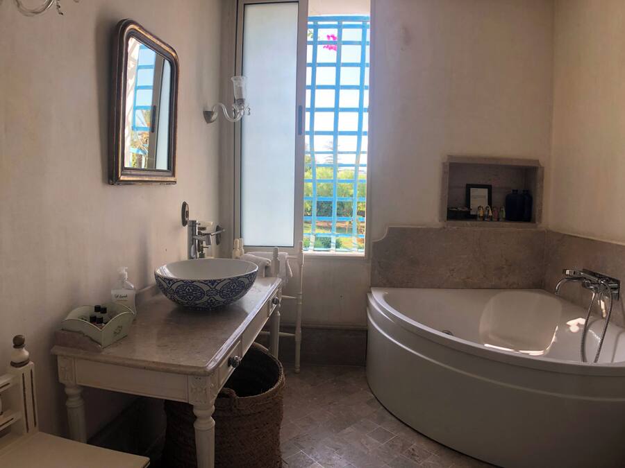 Un baño con una bañera grande, un lavamanos con un cuenco decorativo, un espejo y una ventana con vistas a follaje.