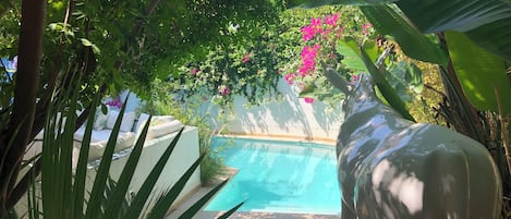 A pool area with a statue of a bull, surrounded by lush greenery and flowering plants.
