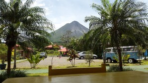 A view of a mountain with a red-roofed building and parked cars in the foreground. - Hotel Fuego Arenal (La Fortuna)
