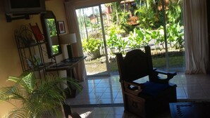 A room with a large window, a wooden chair, a small table, and a potted plant. - Hotel Fuego Arenal (La Fortuna)