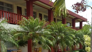 A building with a red and yellow facade, a covered outdoor area with palm trees, and a green lawn. - Hotel Fuego Arenal (La Fortuna)