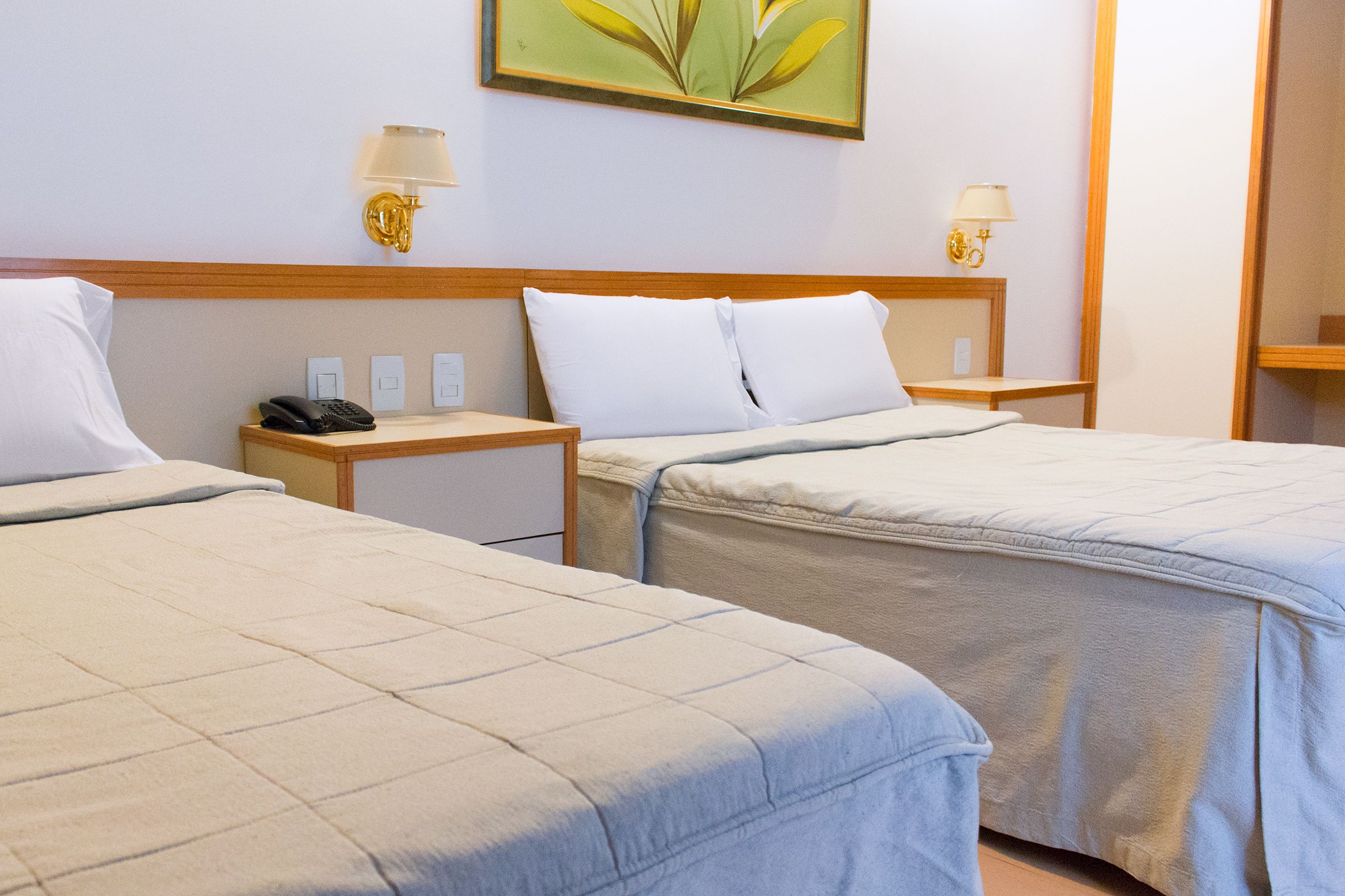 A hotel room with two beds, bedside tables, lamps, and a painting on the wall.