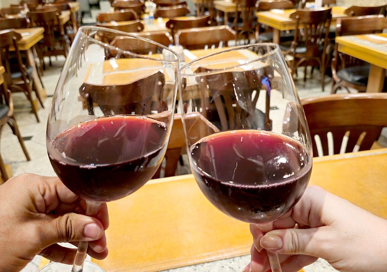 Dos personas sosteniendo copas de vino tinto.