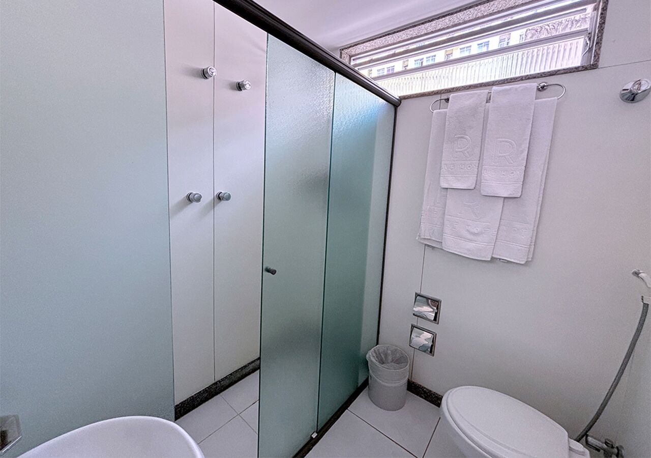 Une salle de bain équipée de toilettes, d’une poubelle, d’un porte-serviettes avec des serviettes et d’une cloison en verre.