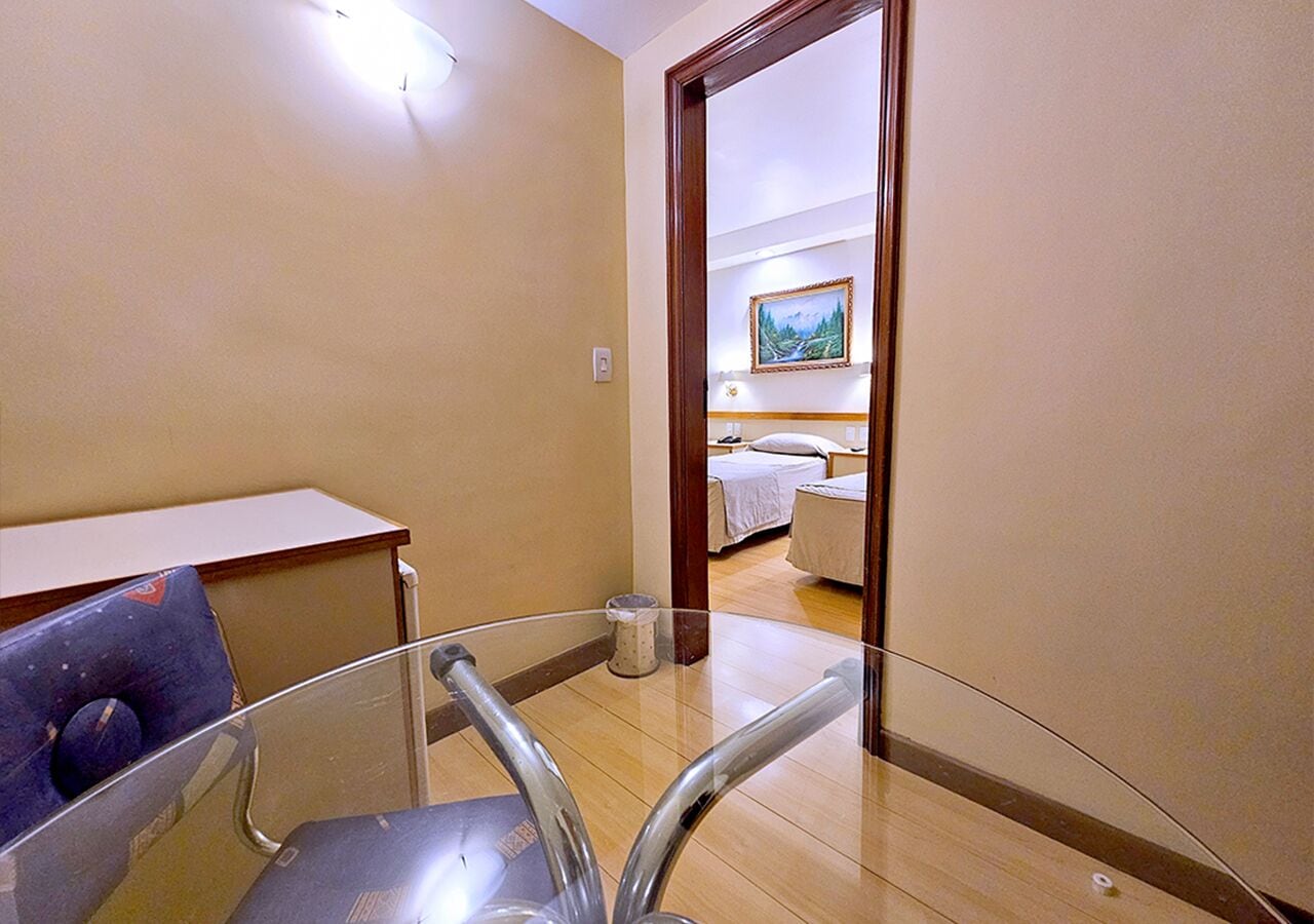 A hotel room with a glass partition, a bed, a bedside table, and a painting on the wall.