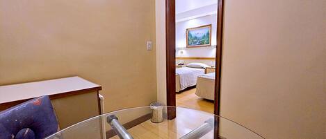A hotel room with a glass partition, a bed, a bedside table, and a painting on the wall.
