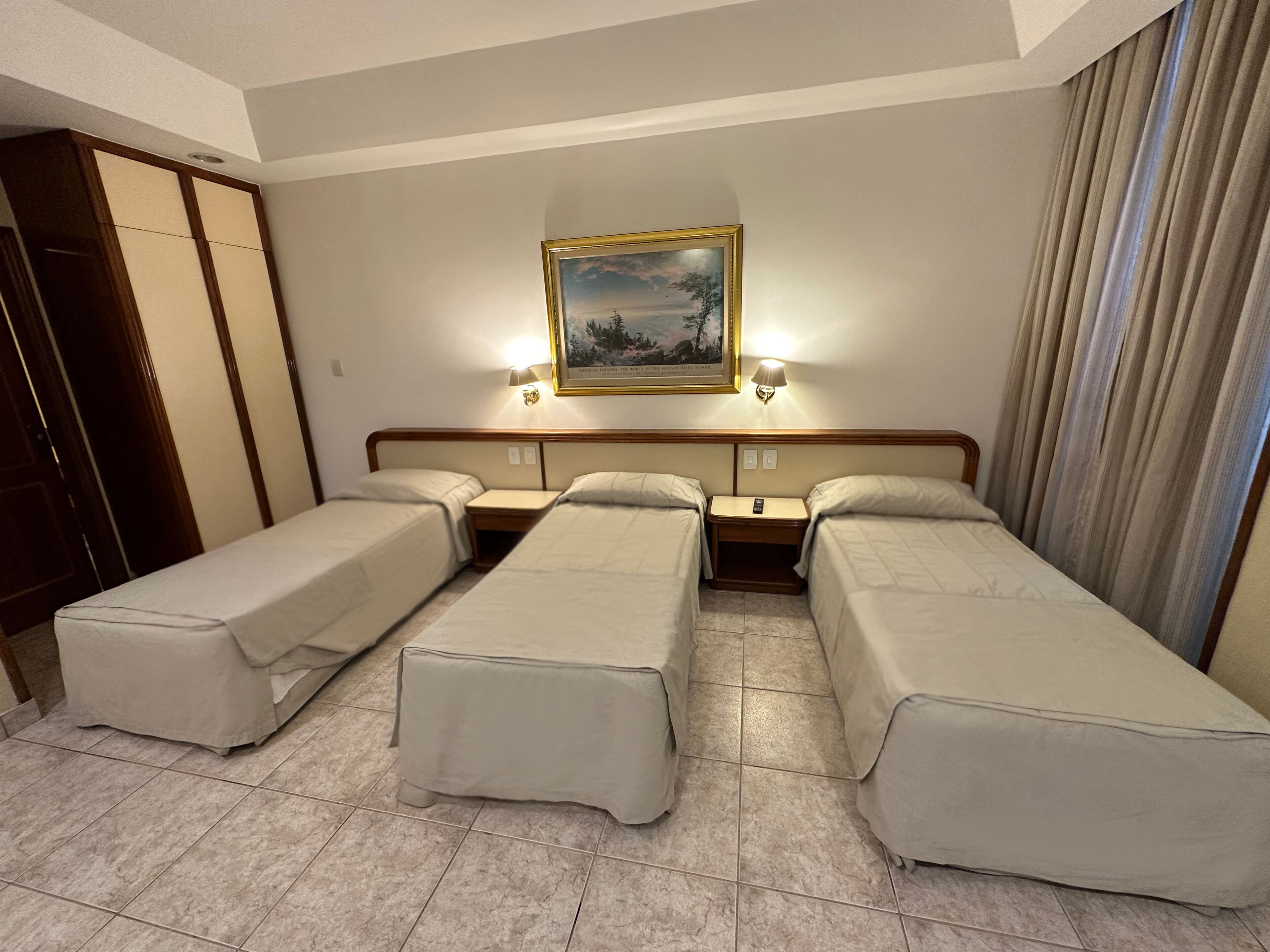Habitación de hotel con dos camas individuales, una mesita de noche con lámpara y un cuadro en la pared.
