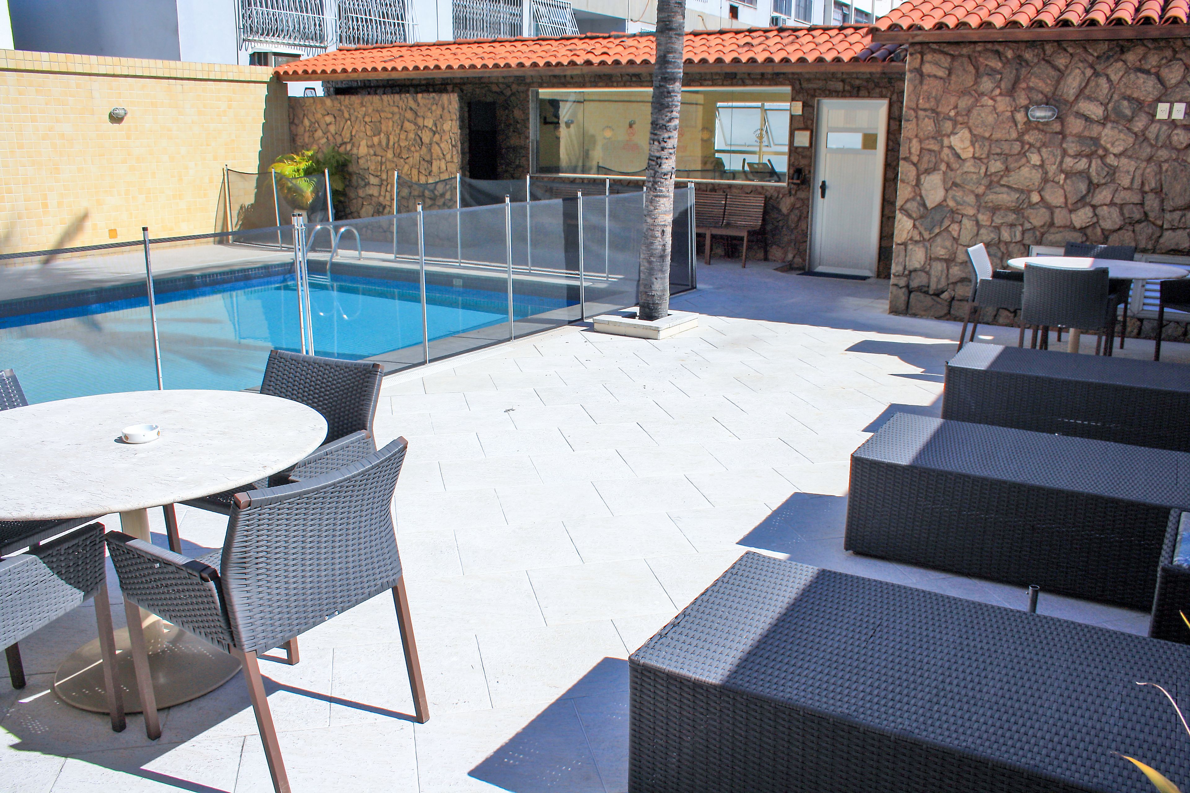 An outdoor pool area with a stone wall, a covered seating area, and a dining table with chairs.