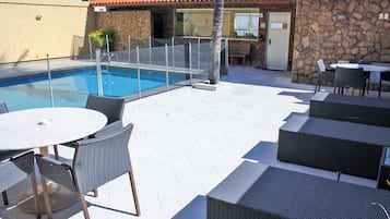 An outdoor pool area with a stone wall, a covered seating area, and a dining table with chairs.