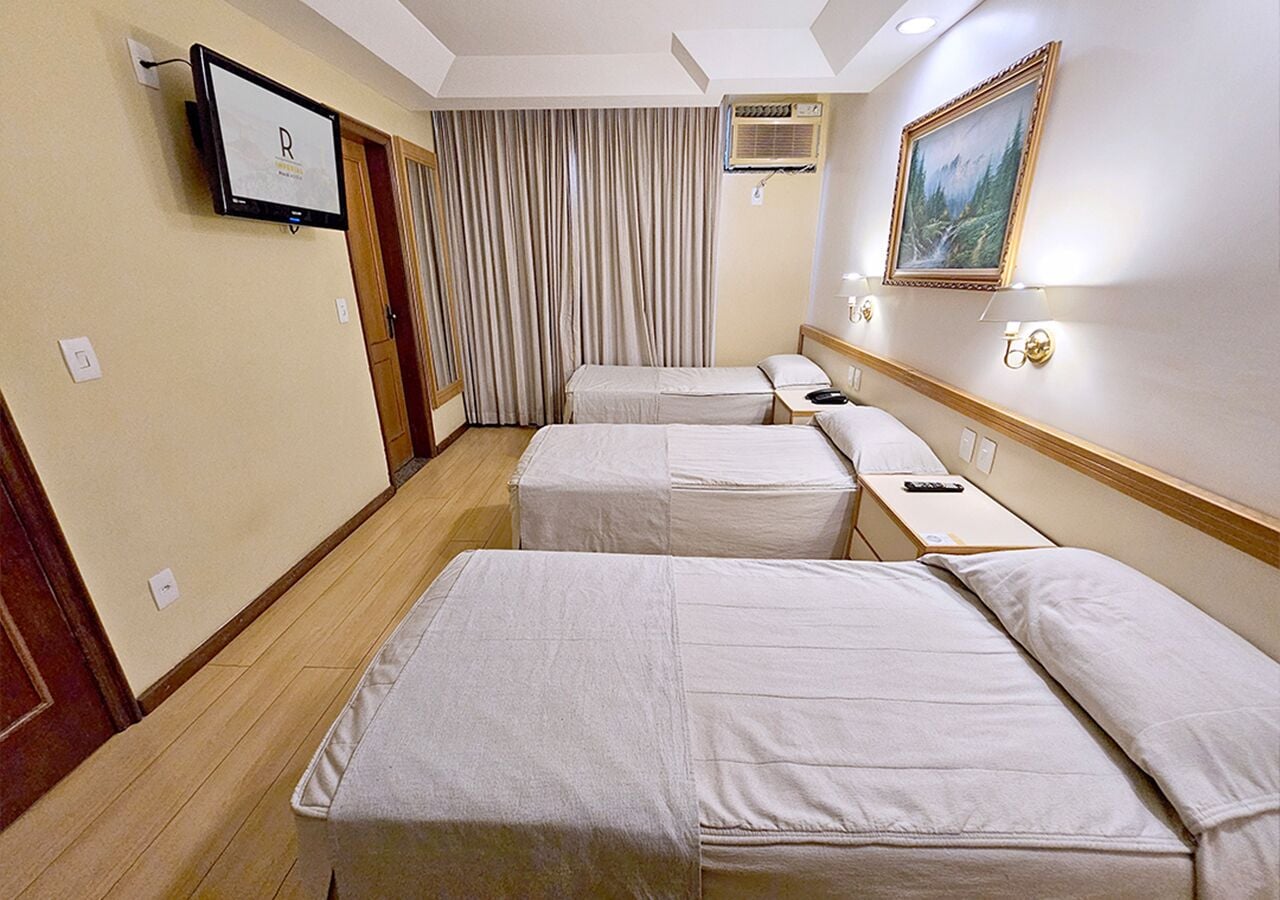 Habitación de hotel con tres camas individuales, un televisor montado en la pared, un cuadro y una ventana con cortinas.