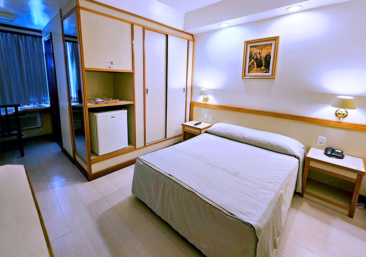 A hotel room with a bed, a wardrobe, a desk, and a bedside table.