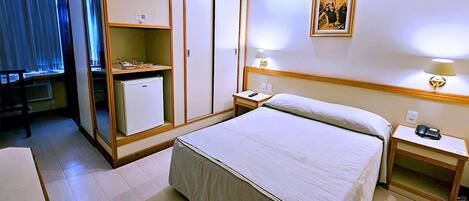 A hotel room with a bed, a wardrobe, a desk, and a bedside table.