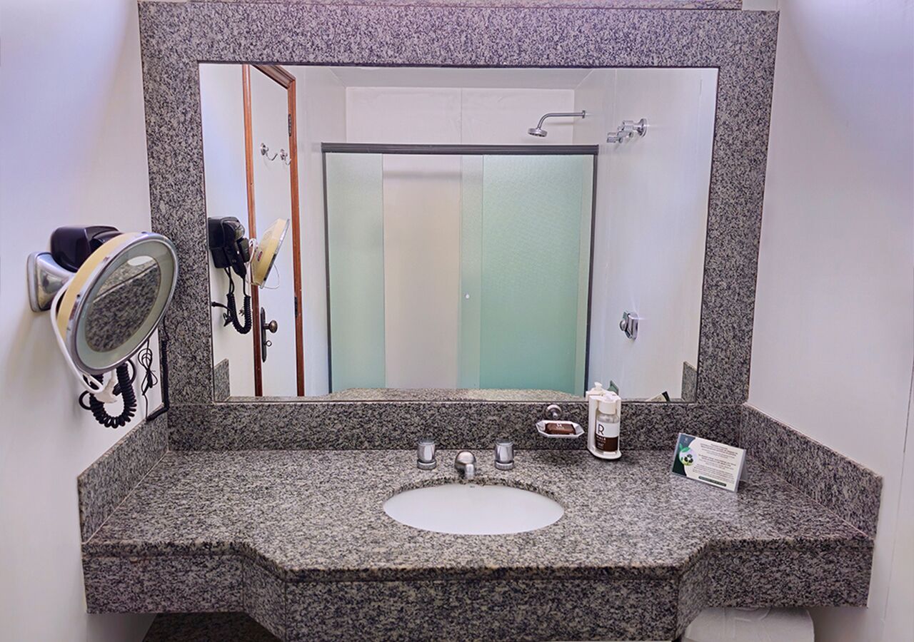 A bathroom with a granite countertop, a white sink, a mirror, a hairdryer, and a soap dispenser.