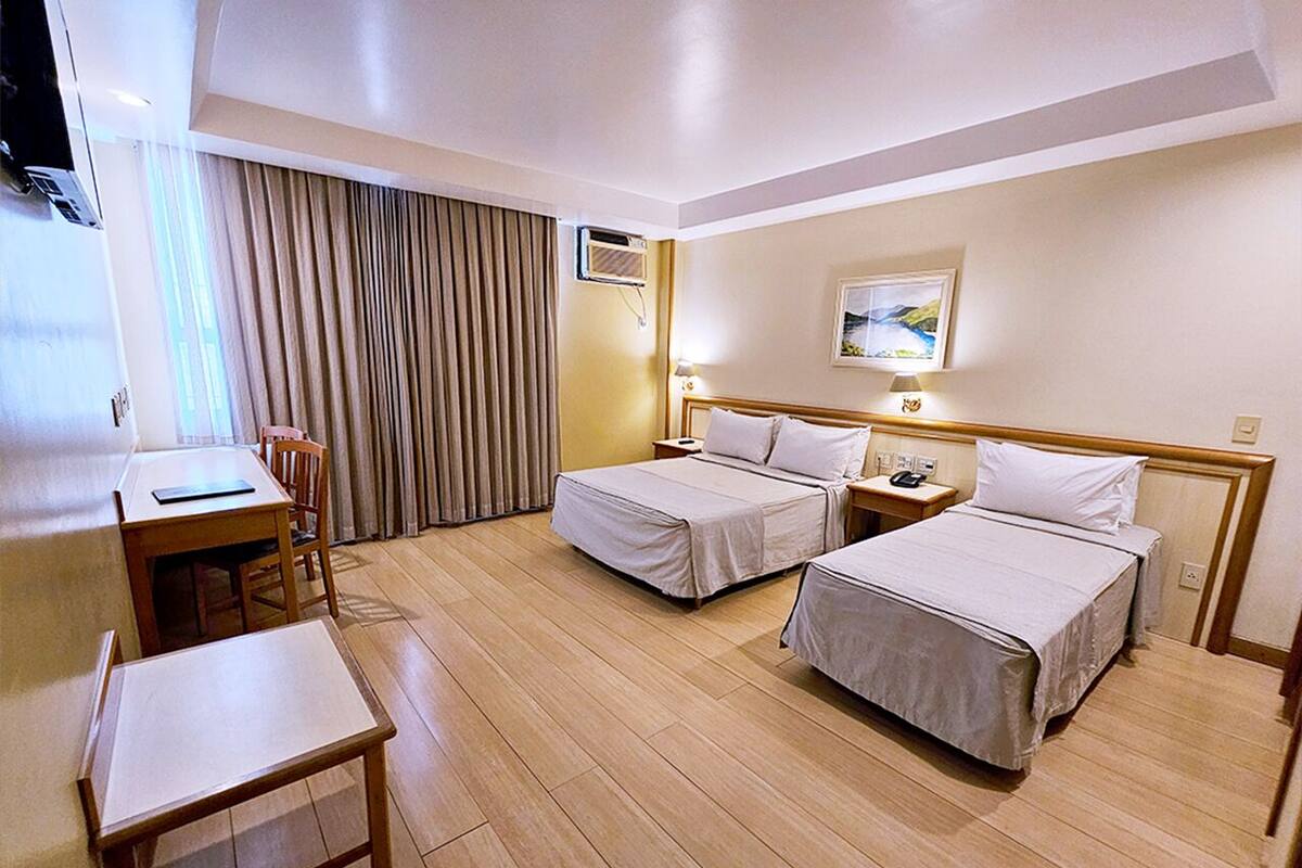 Ein Hotelzimmer mit zwei Betten, einem Schreibtisch, einem Stuhl und einem großen Fenster mit Vorhängen.