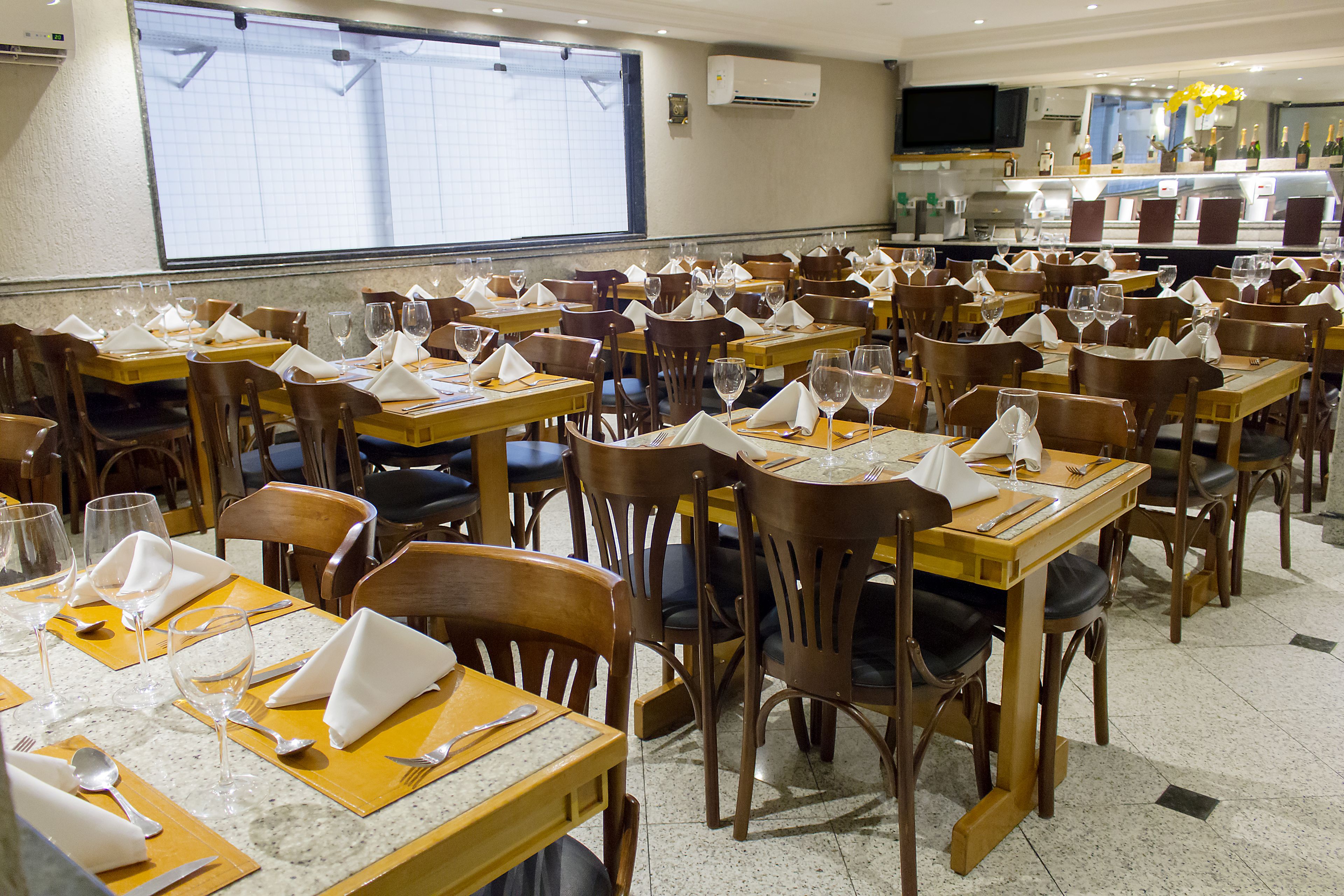 Un restaurante con varias mesas y sillas, cada conjunto con cubiertos y servilletas.