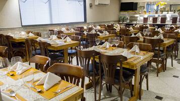 Um restaurante com várias mesas e cadeiras, cada conjunto com talheres e guardanapos.