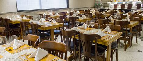 Un restaurante con varias mesas y sillas, cada conjunto con cubiertos y servilletas.