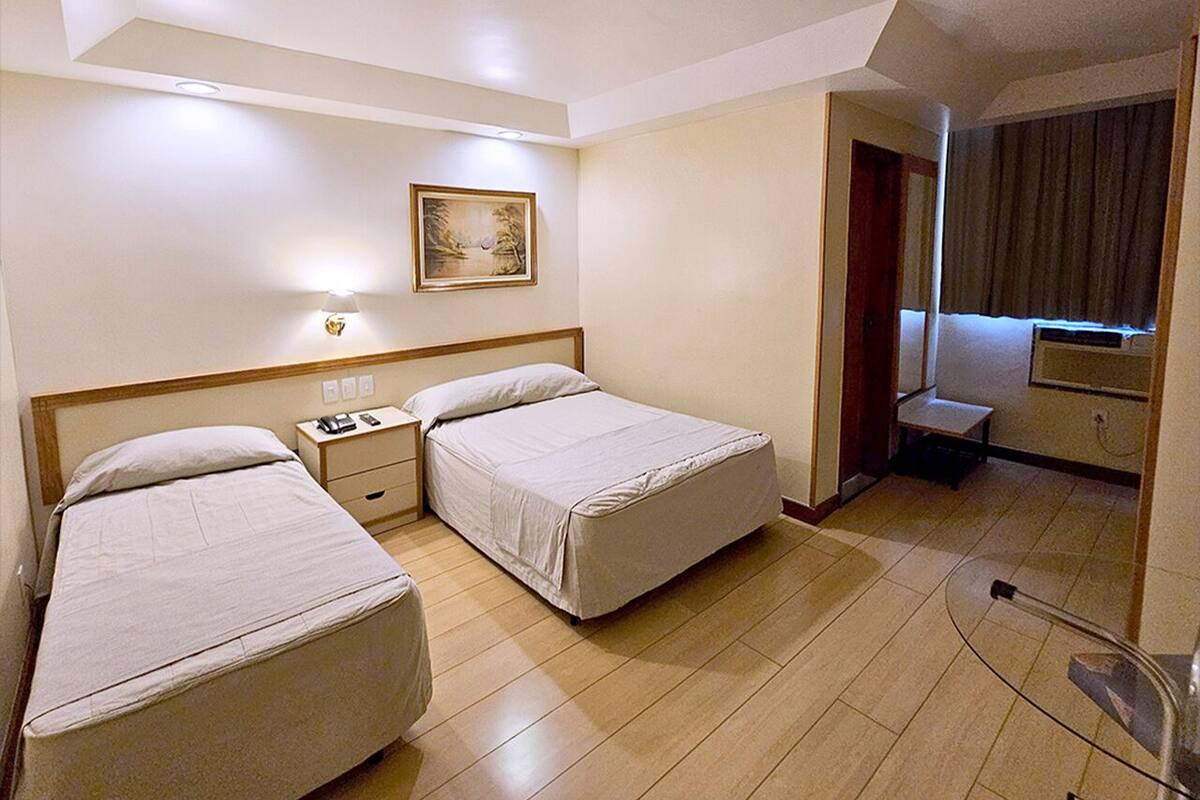 Ein Hotelzimmer mit zwei Betten, einem Nachttisch mit Lampe, einem Bild an der Wand und einer kleinen Sitzecke mit Stuhl und Tisch.