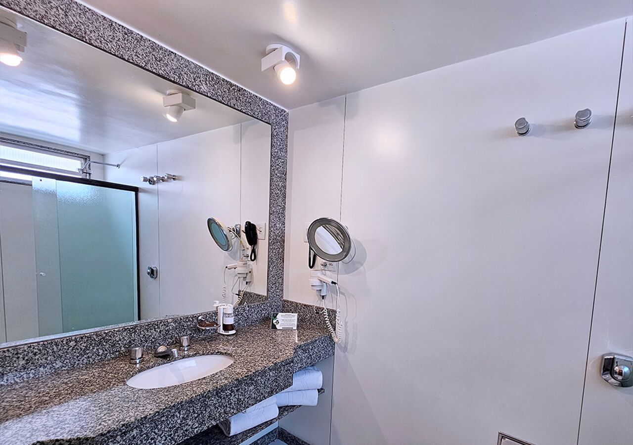 Casa de banho com lavatório de bancada em granito, duas espelhas, secador de cabelo e toalheiro.