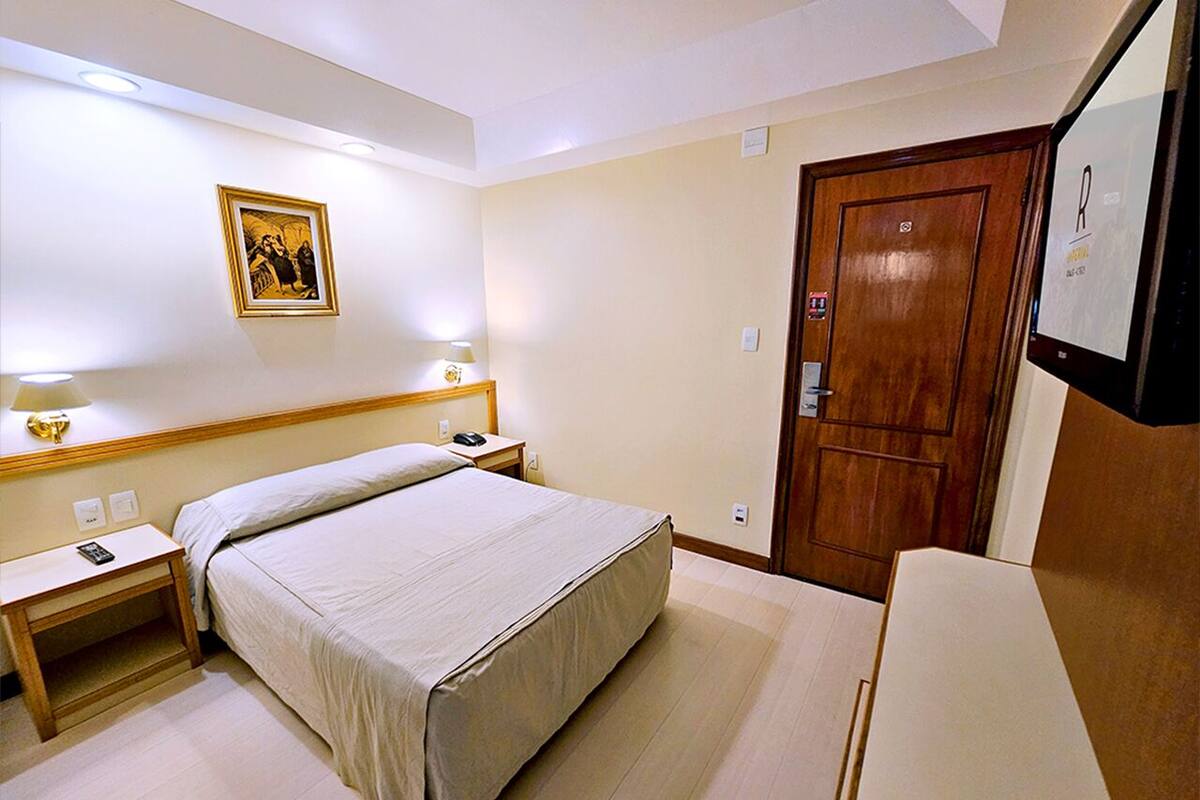 Ein Hotelzimmer mit Bett, Nachttisch, Lampe und einer Holztür.